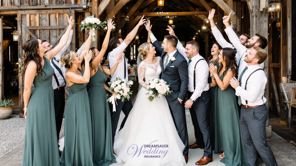 A bride and groom are surrounded by bridesmaids in green and groomsman with green ties celebrating. The couple are looking at each other and everyone is in front of a dark building